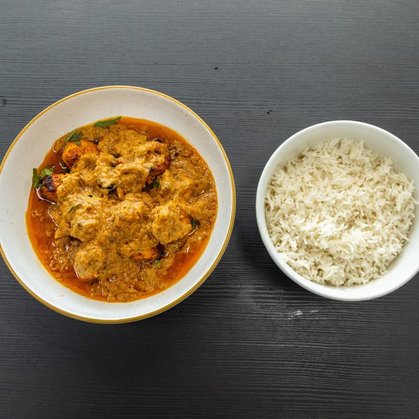 A bowl of chicken tikka masala with cilantro, next to a bowl of white rice on a dark table.