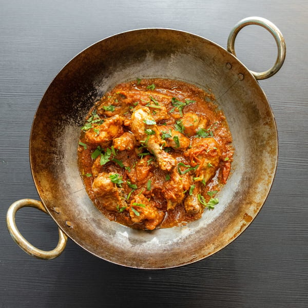 Chicken curry with fresh cilantro in a rustic metal wok on a dark wooden table.