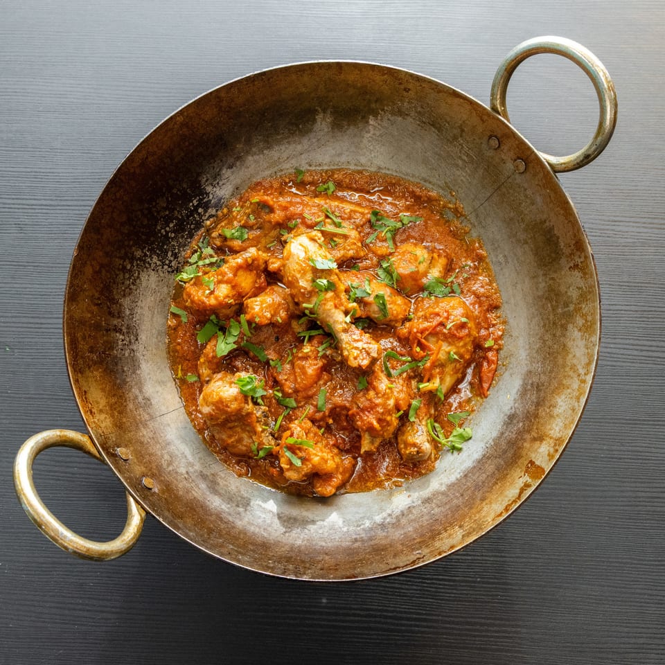 Chicken curry with fresh cilantro in a rustic metal wok on a dark wooden table.