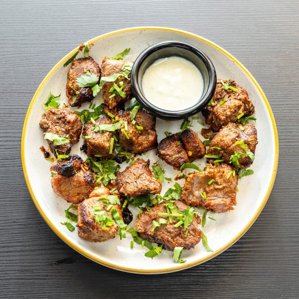 Grilled meat pieces garnished with fresh herbs and a side of white dipping sauce on a plate.