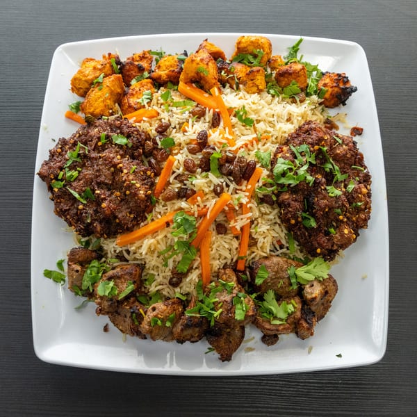 A white rectangular plate filled with rice, meat patties, chicken tikka, and lamb tikka.