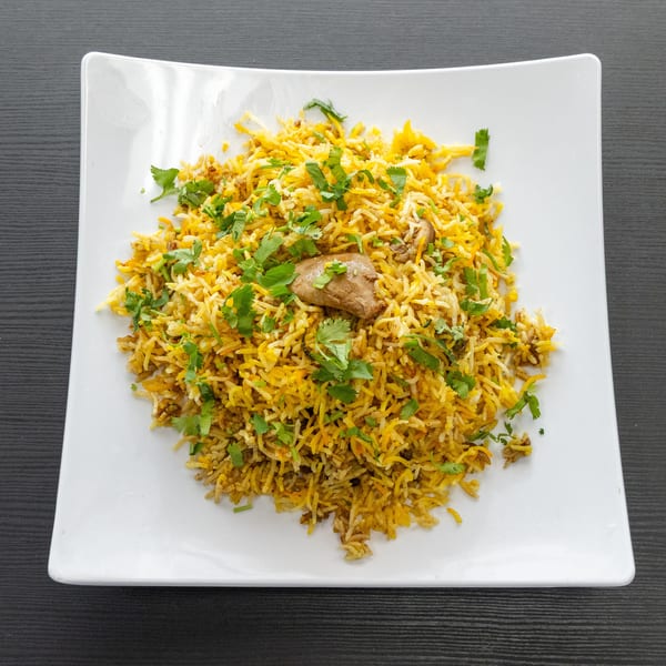 Chicken biryani with cilantro on a white rectangular plate, viewed from above.
